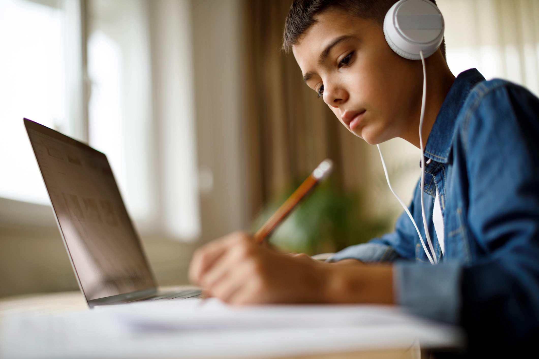 student wearing headphones and doing homework in front of a laptop